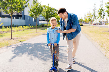 Image showing happy father and little son riding scooter in city