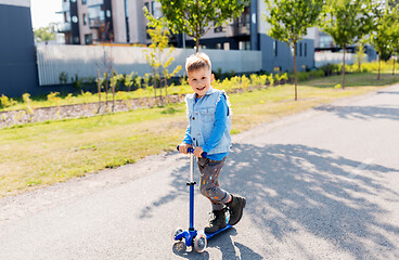 Image showing happy little boy riding scooter in city