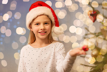 Image showing happy girl in santa hat decorating christmas tree