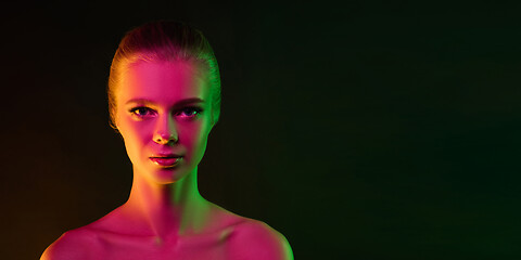 Image showing Portrait of female fashion model in neon light on dark studio background.