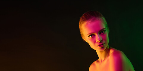 Image showing Portrait of female fashion model in neon light on dark studio background.