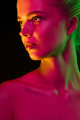 Image showing Portrait of female fashion model in neon light on dark studio background.