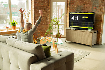 Image showing TV screen with mobile app for betting and score, cheering friends, fans in front of it look excited