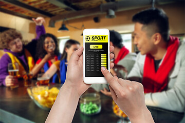 Image showing Device screen with mobile app for betting and score, cheering friends, fans on background