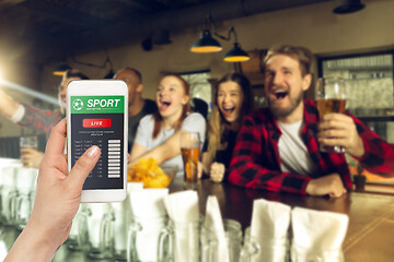 Image showing Device screen with mobile app for betting and score, cheering friends, fans on background
