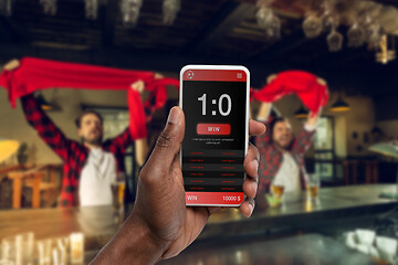 Image showing Device screen with mobile app for betting and score, cheering friends, fans on background