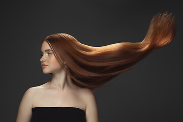 Image showing Beautiful model with long smooth, flying red hair isolated on dark studio background.