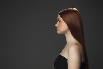 Image showing Beautiful model with long smooth, flying red hair isolated on dark studio background.