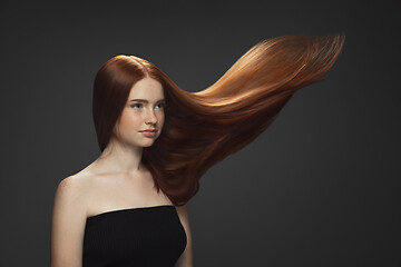 Image showing Beautiful model with long smooth, flying red hair isolated on dark studio background.