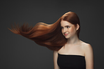 Image showing Beautiful model with long smooth, flying red hair isolated on dark studio background.