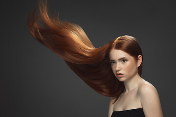 Image showing Beautiful model with long smooth, flying red hair isolated on dark studio background.