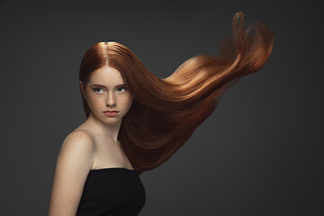 Image showing Beautiful model with long smooth, flying red hair isolated on dark studio background.