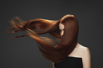 Image showing Beautiful model with long smooth, flying red hair isolated on dark studio background.