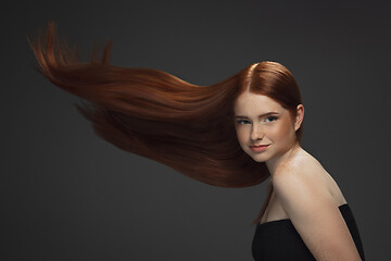 Image showing Beautiful model with long smooth, flying red hair isolated on dark studio background.