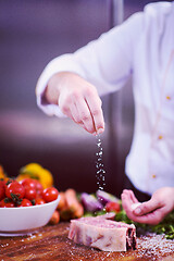 Image showing Chef putting salt on juicy slice of raw steak