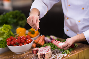 Image showing Chef putting salt on juicy slice of raw steak