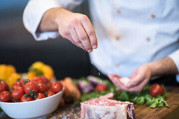 Image showing Chef putting salt on juicy slice of raw steak