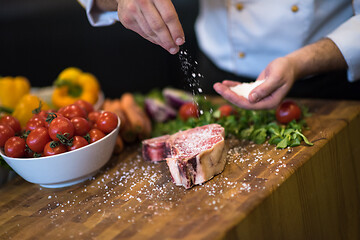 Image showing Chef putting salt on juicy slice of raw steak