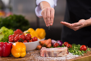 Image showing Chef putting salt on juicy slice of raw steak