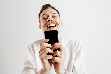 Image showing Young handsome man showing smartphone screen isolated on gray background in shock with a surprise face