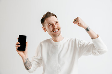 Image showing Young handsome man showing smartphone screen isolated on gray background in shock with a surprise face