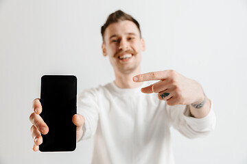 Image showing Young handsome man showing smartphone screen isolated on gray background in shock with a surprise face