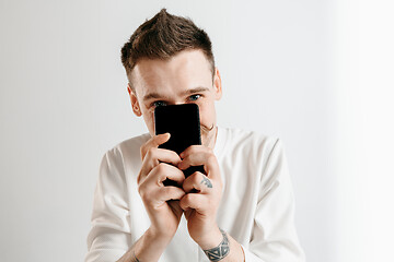 Image showing Young handsome man showing smartphone screen isolated on gray background in shock with a surprise face