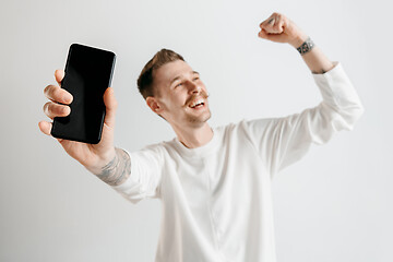 Image showing Young handsome man showing smartphone screen isolated on gray background in shock with a surprise face