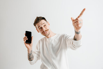 Image showing Young handsome man showing smartphone screen isolated on gray background in shock with a surprise face