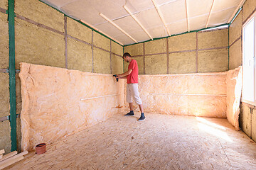 Image showing A worker is installing a roll of insulation in the construction of a country house