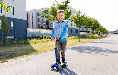 Image showing happy little boy riding scooter in city