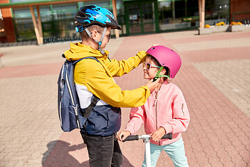 Image showing school boy fastening girl\'s helmet for scooter