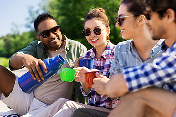 Image showing happy friends drinking tea from thermos in summer