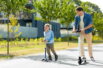 Image showing father and little son riding scooters in city