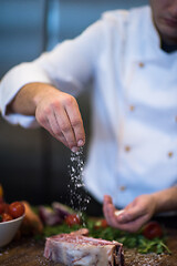 Image showing Chef putting salt on juicy slice of raw steak