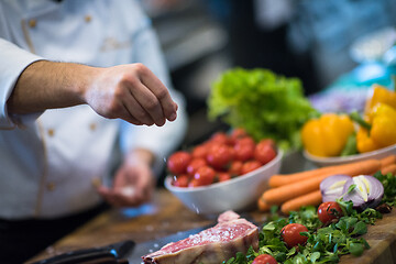 Image showing Chef putting salt on juicy slice of raw steak