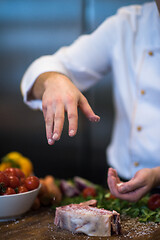 Image showing Chef putting salt on juicy slice of raw steak