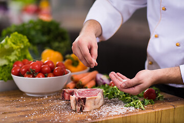 Image showing Chef putting salt on juicy slice of raw steak