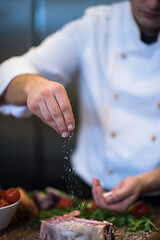 Image showing Chef putting salt on juicy slice of raw steak