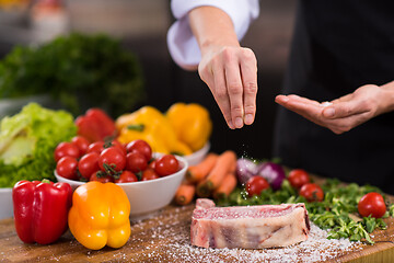 Image showing Chef putting salt on juicy slice of raw steak