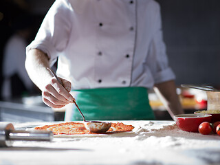 Image showing Chef smearing pizza dough with ketchup