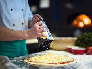 Image showing chef sprinkling cheese over fresh pizza dough