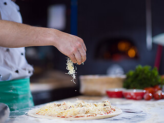 Image showing chef sprinkling cheese over fresh pizza dough