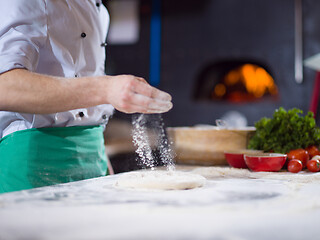 Image showing chef sprinkling flour over fresh pizza dough