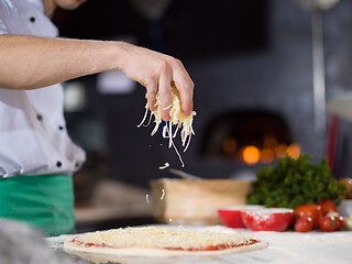 Image showing chef sprinkling cheese over fresh pizza dough