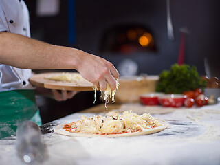 Image showing chef sprinkling cheese over fresh pizza dough