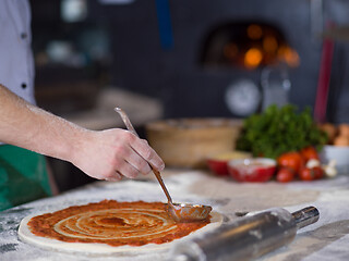 Image showing Chef smearing pizza dough with ketchup