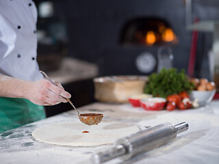 Image showing Chef smearing pizza dough with ketchup