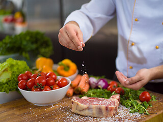 Image showing Chef putting salt on juicy slice of raw steak