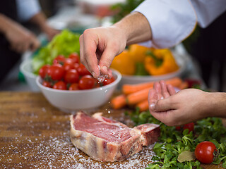 Image showing Chef putting salt on juicy slice of raw steak